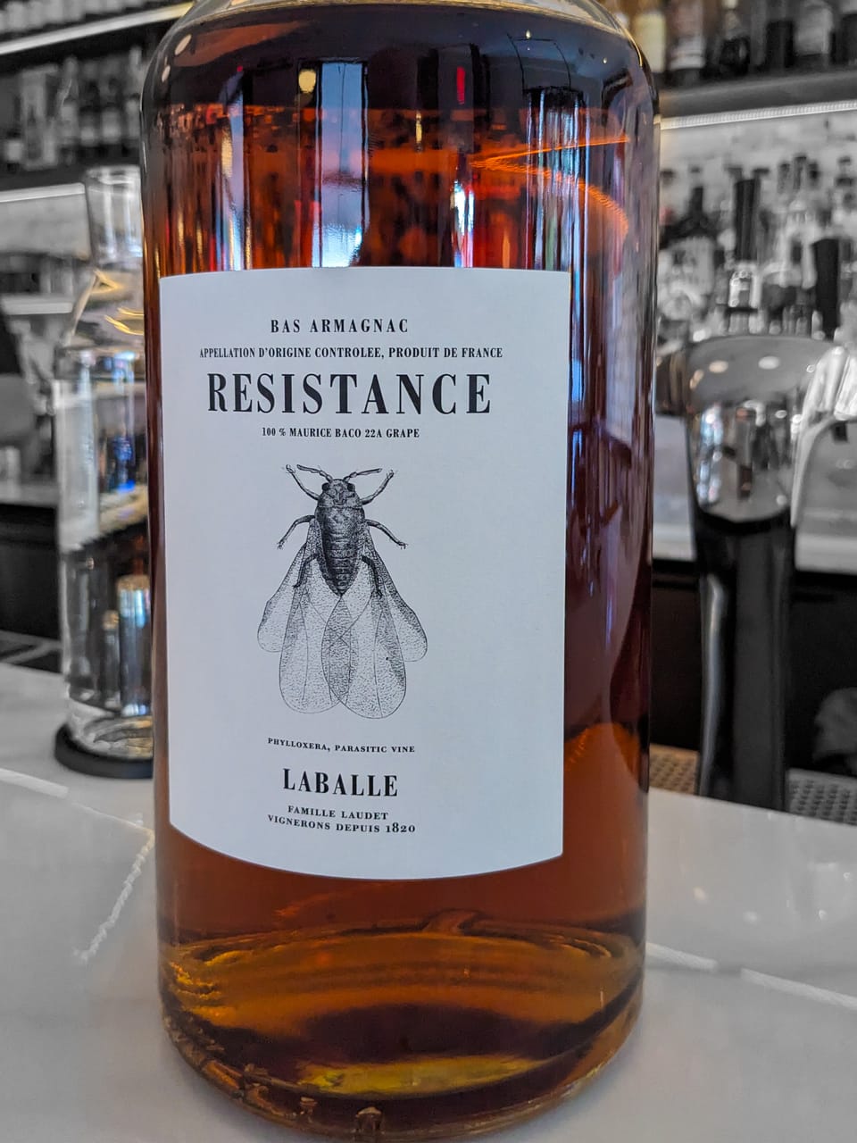 A large bottle of armagnac, with a label reading Resistance, showing a picture of a insect, perhaps a cicada.